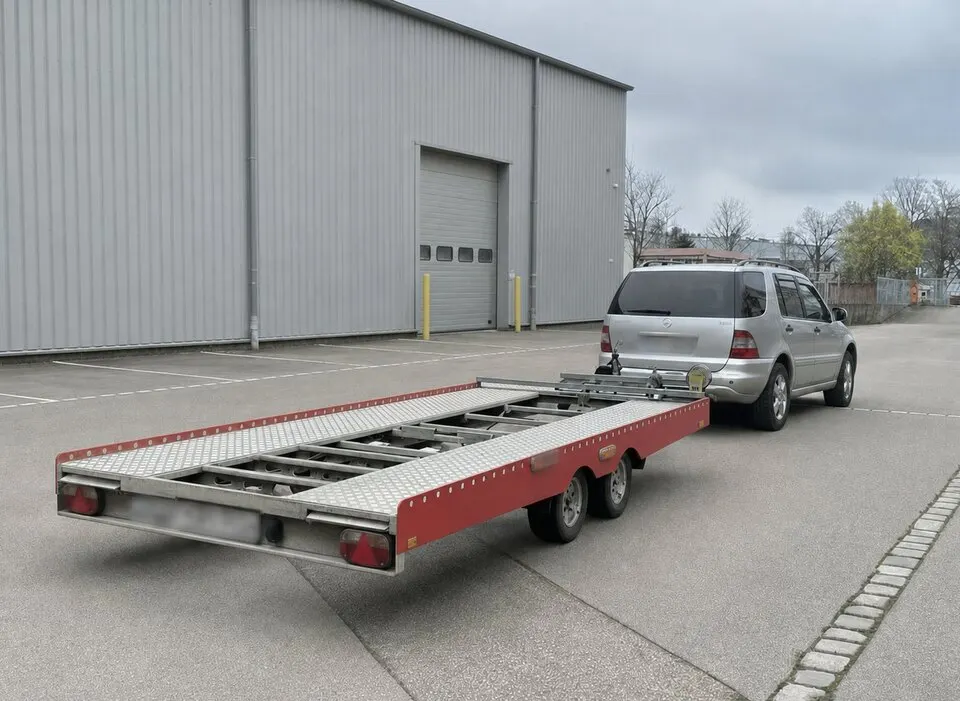 Unsinn-Autotransportanhänger angekuppelt auf einem befestigten Hof
